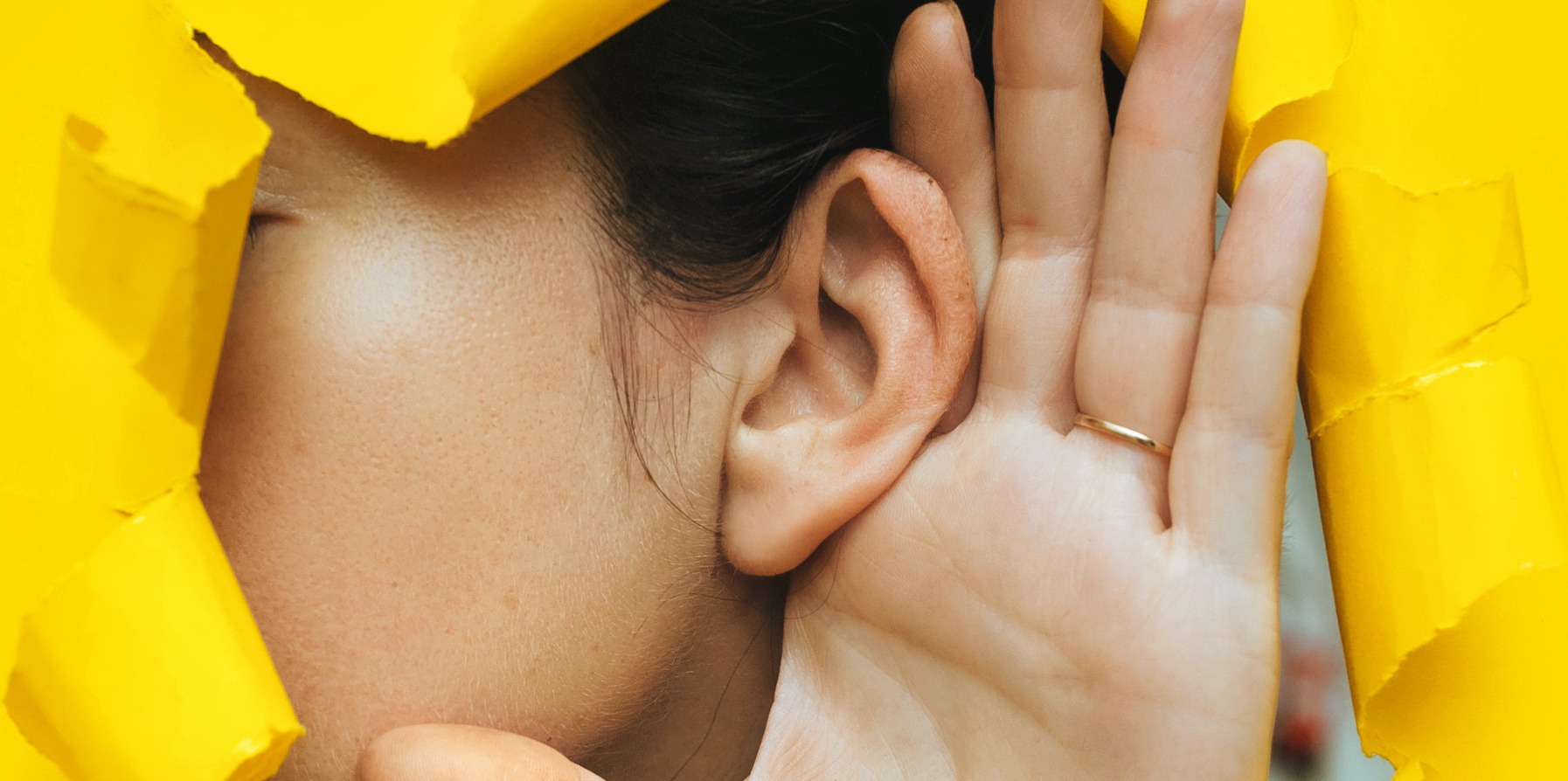 kobiece ucho nadstawione do słuchania na żółtym tle